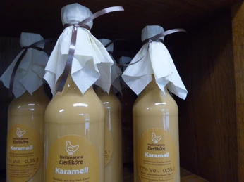 Mehrere Flaschen Heitmanns Karamell-Eierlikör, dekorativ mit Schleife und Tuch auf einem Holzregal.