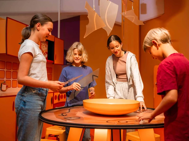 EscapeRoom Vier Kinder experimentieren gemeinsam an einem Tisch in einem kreativen Raum.