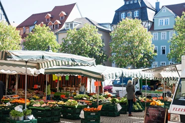 Stand auf dem Jenaer Wochenmarkt mit Kisten voll Gemüse und Obst, dazwischen Kunden und ein Händler