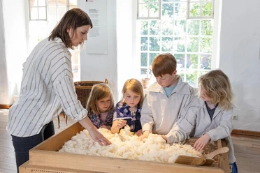 Familienführung im LVR-Industriemuseum Textilfabrik Cromford Eine Gruppe von Kindern erkundet Baumwolle mit einer Begleitperson im LVR-Industriemuseum.