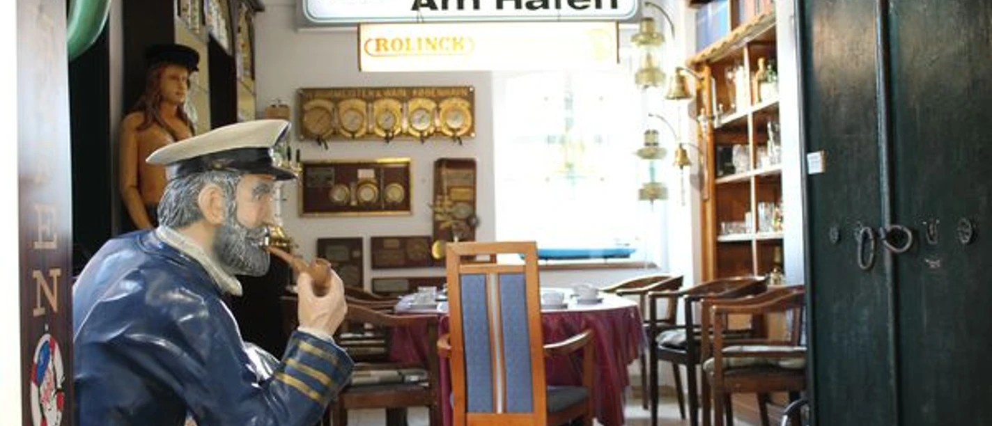 Dätt Haarske Püntker-Patent Haren.jpg Sitzfigur eines Seemanns mit Pfeife in maritim dekoriertem Raum mit Schiffsleuchten und Wandschildern