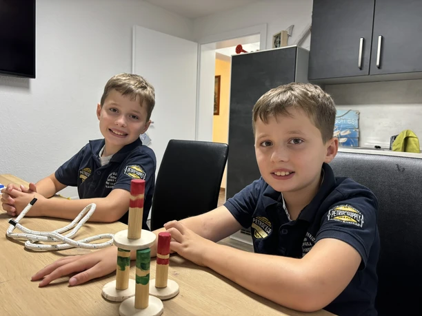 Die Zwillinge Tobias und Lukas sind mit Jonas ihrem großen Bruder Ideengeber von Wasserhelden Emsland.JPEG Zwei Jungen sitzen am Tisch und bauen mit Holzstäben ein kleines Konstruktionsspiel.