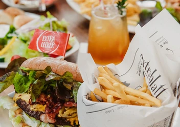 Cafe Extrablatt_PR_19.jpg Burger mit knusprigem Salat und Pommes in Papier gewickelt, begleitet von einem Getränk mit Eiswürfeln.