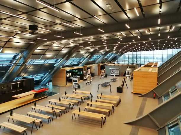 Herford-Bora Flagshipstore_Pro Herford GmbH (3).jpeg Ein moderner Ausstellungsraum mit Holz- und Metalldesign, zahlreichen Sitzbereichen und Bildpräsentationen.