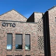 linda&otto Rotes Ziegelgebäude mit modernen grauen Fensterläden und großem Schriftzug "OTTO" an der Fassade.