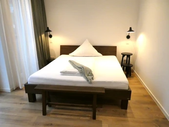 Ein minimalistisches Schlafzimmer mit einem Doppelbett, Holzboden, zwei Wandleuchten und verdeckten Vorhängen.A minimalist bedroom with a double bed, wooden floor, two wall lights and concealed curtains.Et minimalistisk soveværelse med dobbeltseng, trægulv, to væglamper og skjulte gardiner.Een minimalistische slaapkamer met een tweepersoonsbed, houten vloer, twee wandlampen en verborgen gordijnen.