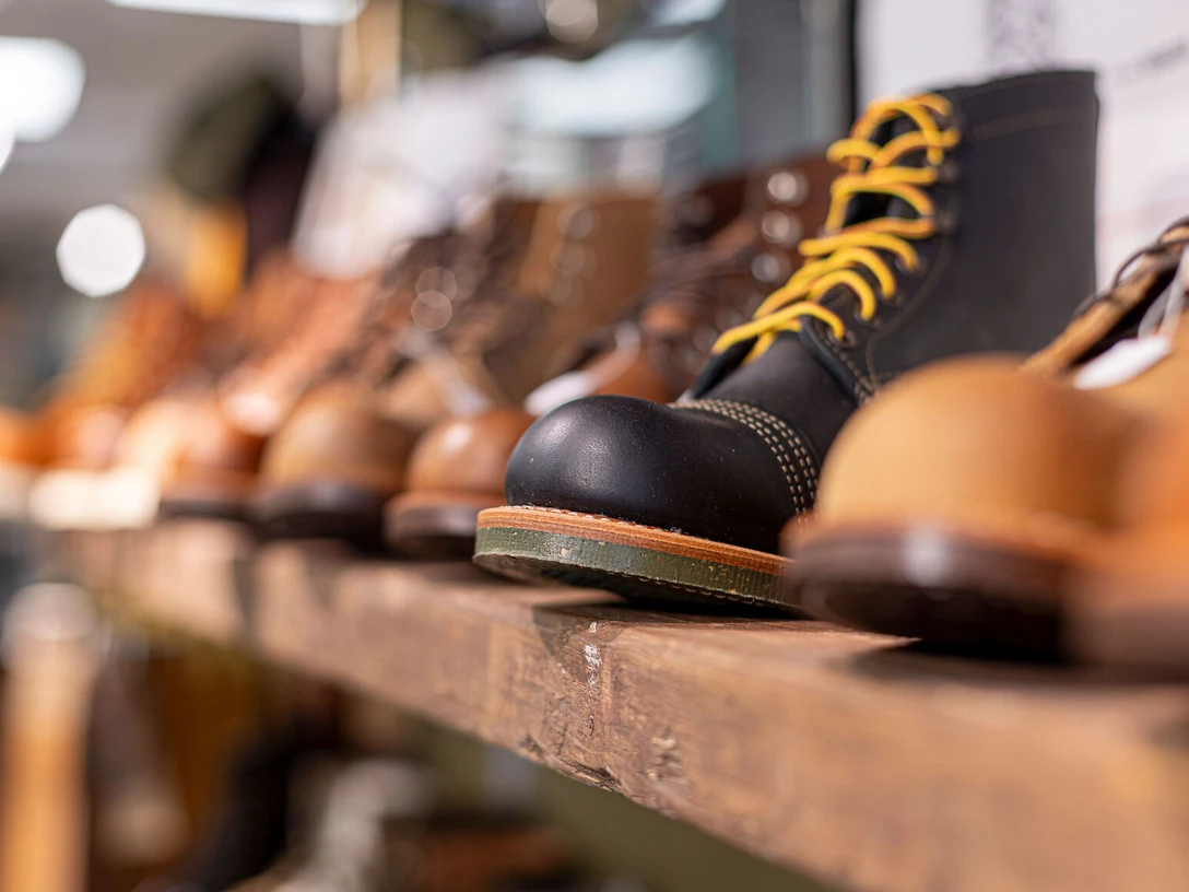 Hochwertige Herrenstiefel im "Herrenzimmer" in der Neuen Straße, Celler Altstadt Eine Nahaufnahme von hochwertigen Herrenstiefeln mit gelben Schnürsenkeln, die in einem Regal im Geschäft "Herrenzimmer" in der Neuen Straße der Celler Altstadt ausgestellt sind. Die Stiefel sind auf einem rustikalen Holzboden platziert.