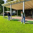 Driving Range im Golfpark Herford-IMG_20210918_111321-BloggerWG-Pro Herford GmbH.jpg Zwei Personen üben ihren Golfschwung auf der Driving Range im Golfpark Herford unter einem Vordach.