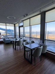 image00004.jpeg Moderner Café-Innenraum mit großen Fenstern, die einen Blick auf eine ruhige Küstenlandschaft bieten.