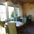 Pension Haus Marbeke Frühstücksraum.jpg Ein lichtdurchfluteter Frühstücksraum mit grünen Polsterstühlen und runden Holztischen.