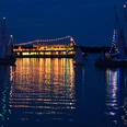 lichternacht-im-kurpark-weisse-flotte-seerundfahrt Eine festlich beleuchtete Fähre strahlt nachts auf einem ruhigen See, umgeben von reflektierenden Segelbooten.