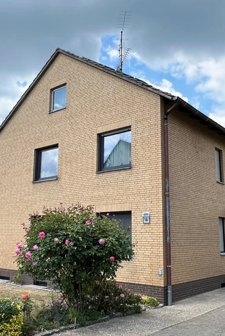 Gemütliches zweistöckiges Backsteinhaus mit gepflegtem Vorgarten, umgeben von hohen Bäumen.