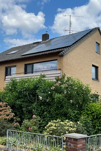 Ein zweigeschossiges Gebäude aus hellen Backsteinen mit Dachsolaranlagen und umgeben von üppigem Grün.
