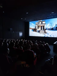 Drum Machines Sicht in einen belegten Kinosaal. Die Zuschauer*innen betrachten die Leinwand auf der ein Film läuft.