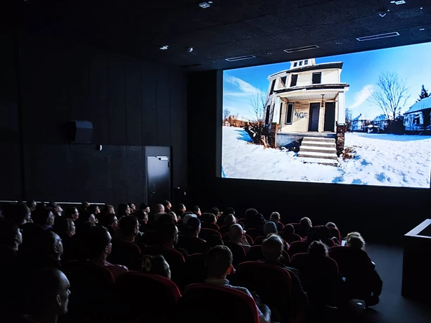 Drum Machines Sicht in einen belegten Kinosaal. Die Zuschauer*innen betrachten die Leinwand auf der ein Film läuft.