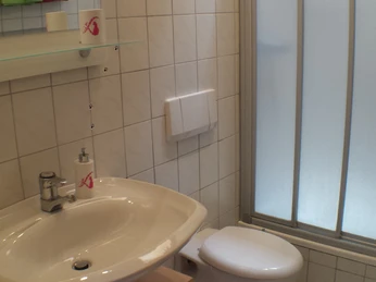 Badezimmer der Ferienwohnung Udo Katzenberger Das Foto zeigt ein Badezimmer mit beigem Waschbecken, Duschkabine mit Einstieg und weißen Fliesen.