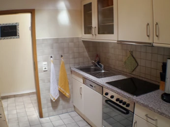 Küche der Ferienwohnung Udo Katzenberger Beigefarbene Küchenzeile mit Herd, Ceranfeld, Mikrowelle, Geschirrspüler und Hängeschränken.