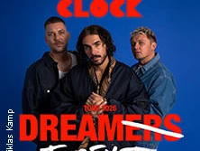 Drei Musiker posieren vor einem blauen Hintergrund mit der Aufschrift "Dreamers Forever Tour 2024".