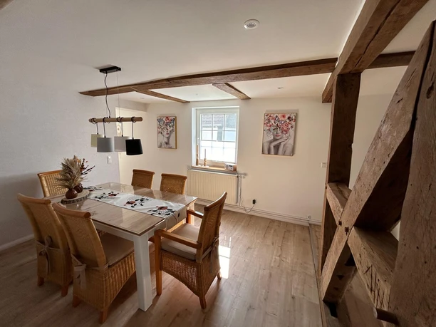 Esszimmer der Ferienwohnung Wesertraum Lauenförde Esstisch aus Holz, sechs Rattanstühle, Hängelampe, zwei Bilder an der Wand, sichtbare Holzbalken