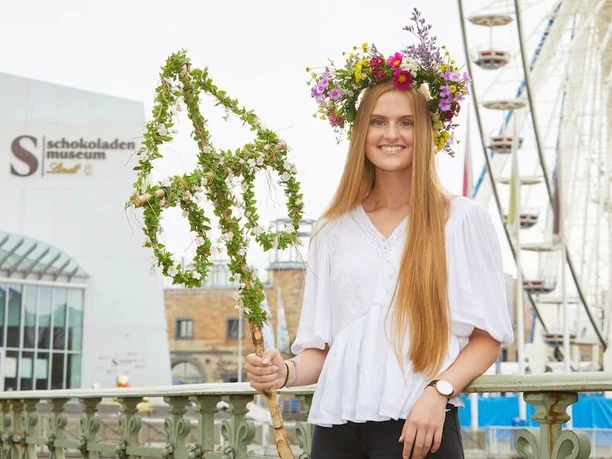 Midsummer festival at the Cologne Chocolate Museum A smiling young woman with a wreath of flowers stands in front of the Chocolate Museum in Cologne. A Ferris wheel can be seen in the background.