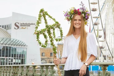 Mittsommerfest am Kölner Schokoladenmuseum Eine lächelnde junge Frau mit Blumenkranz steht vor dem Kölner Schokoladenmuseum. Im Hintergrund ist ein Riesenrad zu sehen.