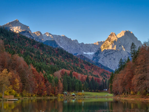Riessersee_im_Herbst_© Markt Garmisch-Partenkirchen_MarcHohenleitner.jpg Herbstfarben am Riessersee mit spiegelndem Wasser und sonnenbeschienenen Berggipfeln