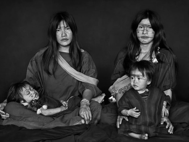 Amazonia Sebastiao Salgado An indigenous family. Two adults sit in the center while two children rest on them. The faces are painted with traditional patterns. An expression of calm and cohesion dominates the scene.