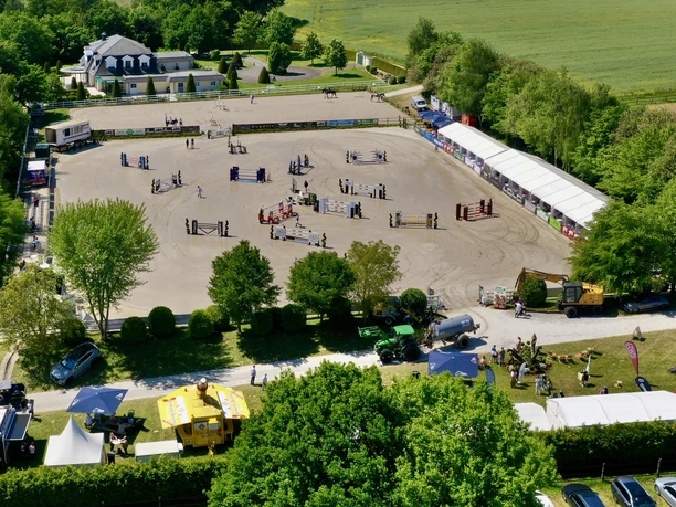 Turniergelände_Foto Viviann Klemm.jpg Luftaufnahme eines Turniergeländes mit Pferdesprungparcours, umgeben von Bäumen und Zelten.