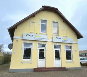 Aussenansicht Haus Pizza 2400 Aussenansicht eines zweistöckigen gelben Gebäudes mit Pizza-Werbung und zwei Eingängen.