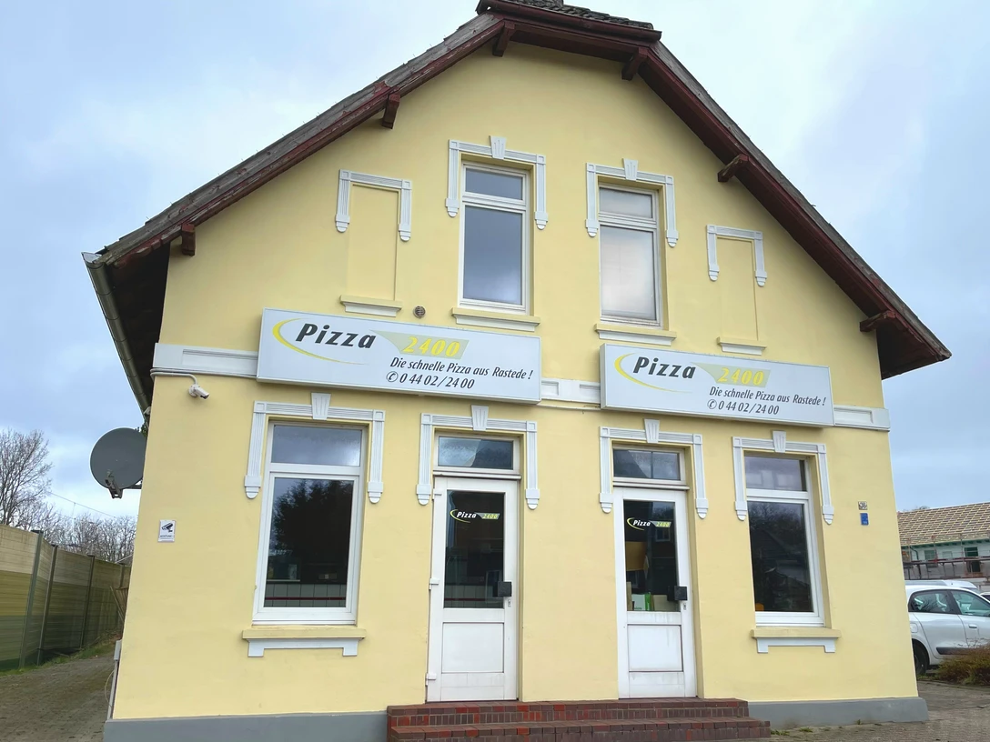 Aussenansicht Haus Pizza 2400 Aussenansicht eines zweistöckigen gelben Gebäudes mit Pizza-Werbung und zwei Eingängen.