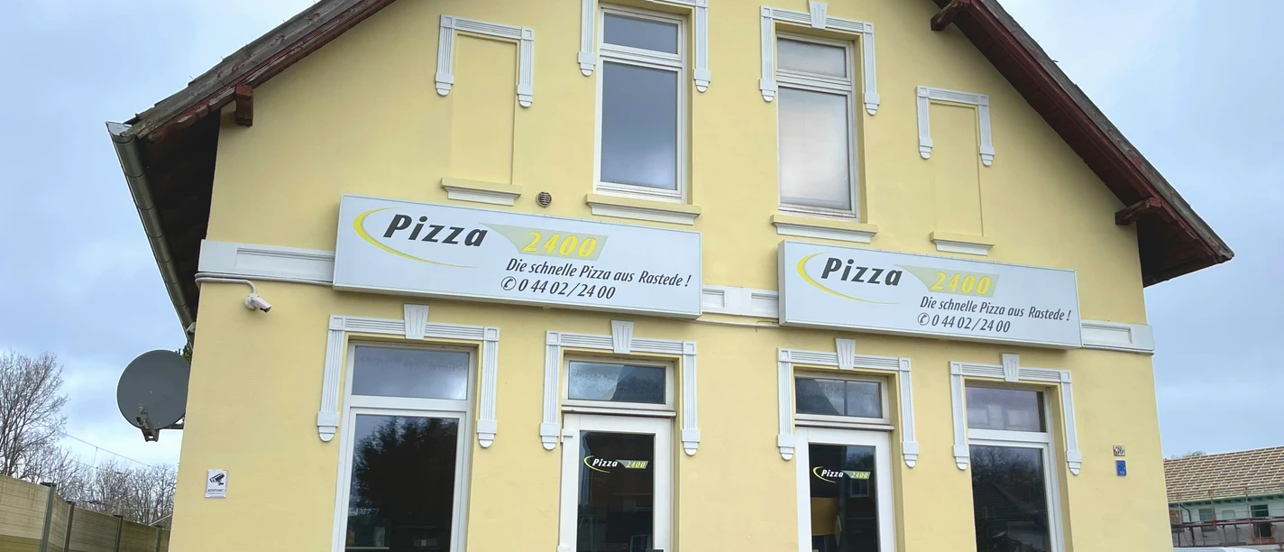 Aussenansicht Haus Pizza 2400 Aussenansicht eines zweistöckigen gelben Gebäudes mit Pizza-Werbung und zwei Eingängen.