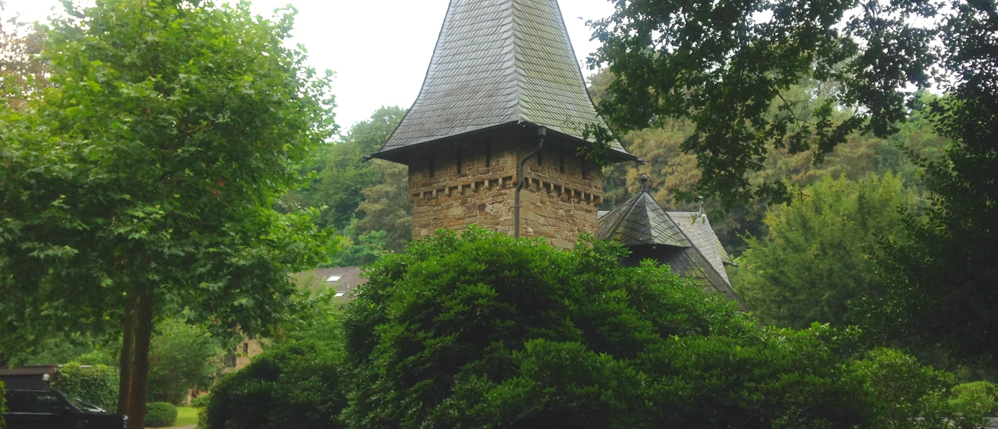 Schloss Caspersbroich von Außen (Privatbesitz) Schloss Caspersbroich in Solingen mit Türmen und üppigem Grün umgeben, steht inmitten dichter Vegetation.