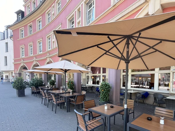 Café Fritzenkötter Straßencafé mit Holztischen und Sonnenschirmen vor einer rosafarbenen Gebäudefassade.