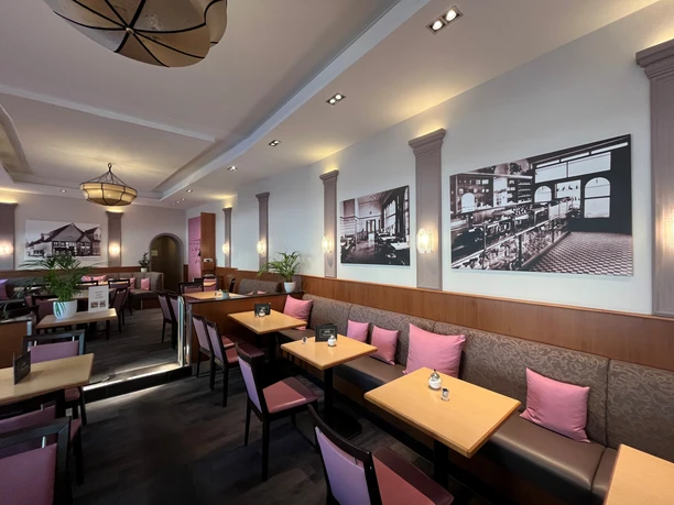 Café Fritzenkötter Gemütliches Café mit moderner Einrichtung, Holztischen, rosa Kissen und historischen Fotografien an den Wänden.