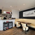 2025-05-23 Eiscafe Ferreira.jpg Ein gemütliches Café mit moderner Einrichtung, Thekenbereich und stilvollem Sitzbereich.