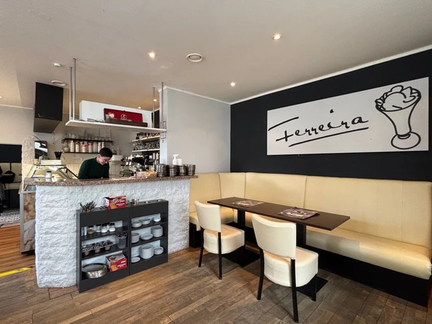 2025-05-23 Eiscafe Ferreira.jpg Ein gemütliches Café mit moderner Einrichtung, Thekenbereich und stilvollem Sitzbereich.