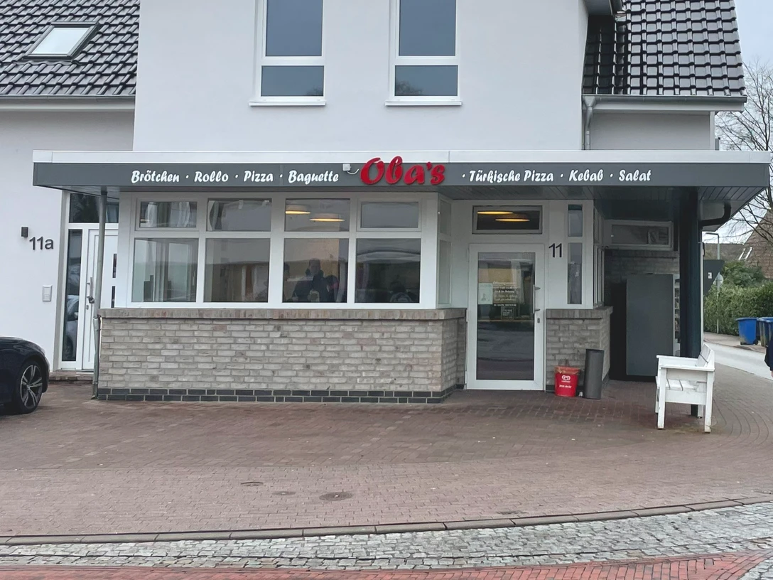 Aussenansicht Oba's Das Bild zeigt einen modernen Dönerladen mit einem hellen, weißen Außenanstrich. Über der Eingangstür prangt ein Schild mit der Aufschrift "Obas's".