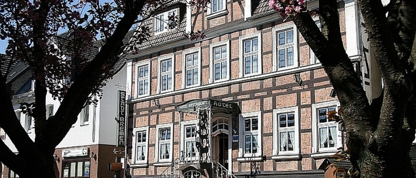 Hotel Stadt Bremen Historisches Fachwerkgebäude mit blühenden Bäumen im Vordergrund, zentrale Treppe zum Eingang.