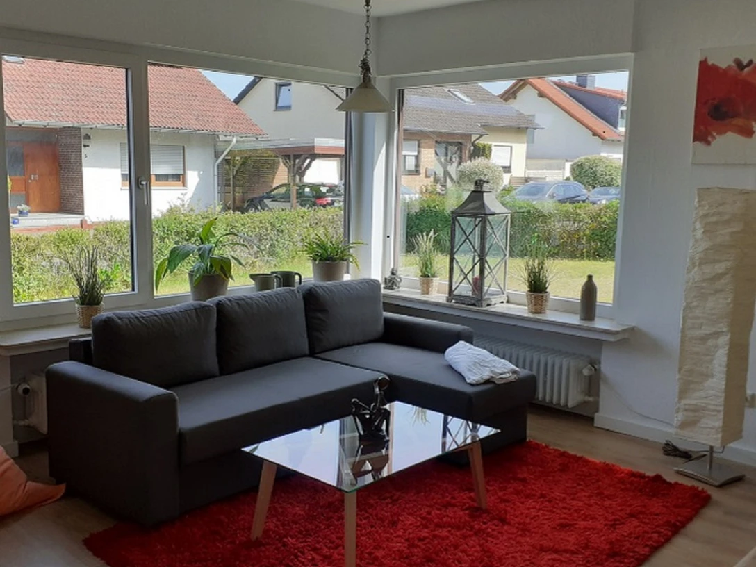 Ferienwohnung Voetter Wohnzimmer mit großer Fensterfront, Zimmerpflanzen auf der Fensterbank, grauem modernen Sofa, Glastisch