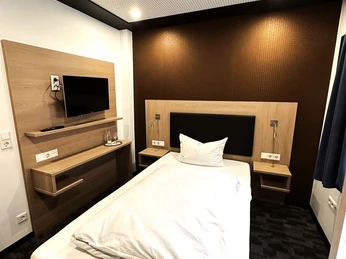 Einzelzimmer des Hotels Asado Einzelzimmer im Hotel Asado: Weißes Bett, schwarzer Boden, Leselampe, Fernseher.