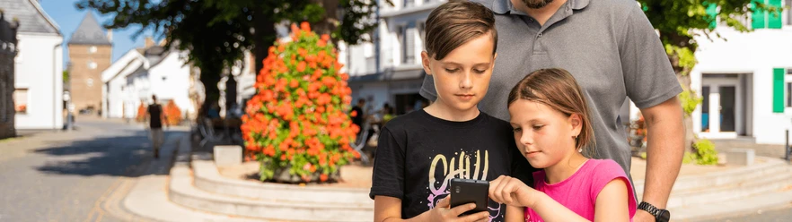 Stadtrallye mit Familie Eine Familie erkundet gemeinsam eine Stadtrallye. Zwei Kinder fokussieren sich auf ein Smartphone.