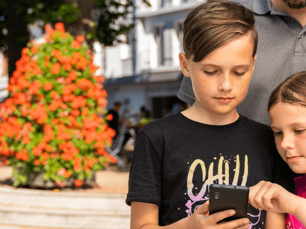 Stadtrallye mit Familie Eine Familie erkundet gemeinsam eine Stadtrallye. Zwei Kinder fokussieren sich auf ein Smartphone.