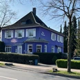Café Clärchen in Velbert, Außenansicht Älteres, lila Gebäude mit weiß umrahmten Fenstern, umgeben von Bäumen und Hecken in Velbert.