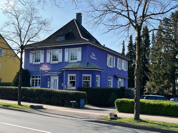 Café Clärchen in Velbert, Außenansicht Älteres, lila Gebäude mit weiß umrahmten Fenstern, umgeben von Bäumen und Hecken in Velbert.