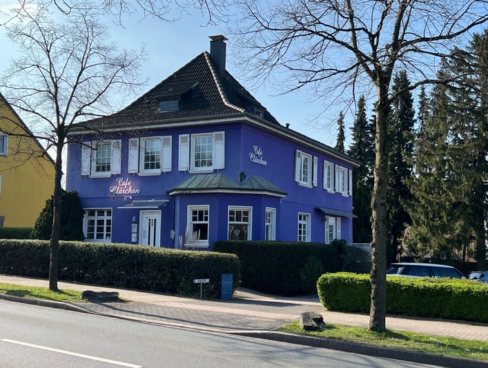 Café Clärchen in Velbert, Außenansicht Älteres, lila Gebäude mit weiß umrahmten Fenstern, umgeben von Bäumen und Hecken in Velbert.