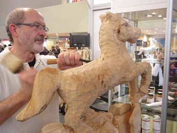 Deutsches Kreativzentrum Holz Ein handwerklich versierter Mann schnitzt mit Hammer und Meißel an einer detaillierten Holzskulptur eines Pferdes in einem kreativen Studio.