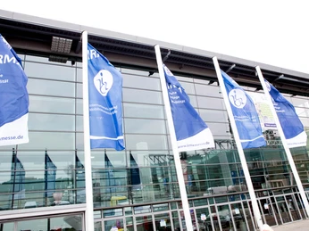 Halle-und-Flaggen-©-Escales-Verlag.jpg Flaggen wehen vor der Messehalle.Flags fly in front of the exhibition hall.Před výstavní halou vlají vlajky.Przed halą wystawową powiewają flagi.Vlaggen wapperen voor de tentoonstellingshal.Le bandiere sventolano davanti alla sala espositiva.