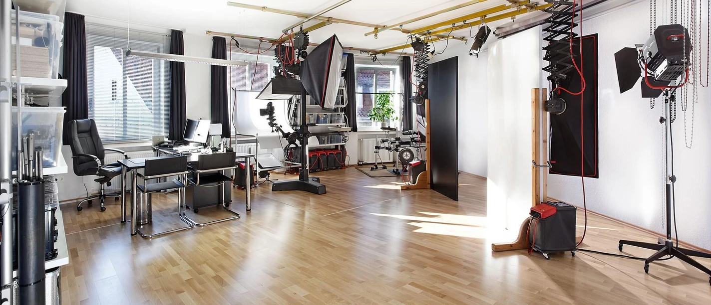 Helles Fotostudio mit Kameras, Blitzanlagen, Softboxen und Arbeitsbereich auf Holzboden