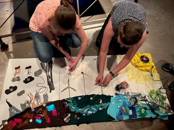 re:create Windmühlen Bild Two women design a creative work of art with colorful materials lying on the floor.