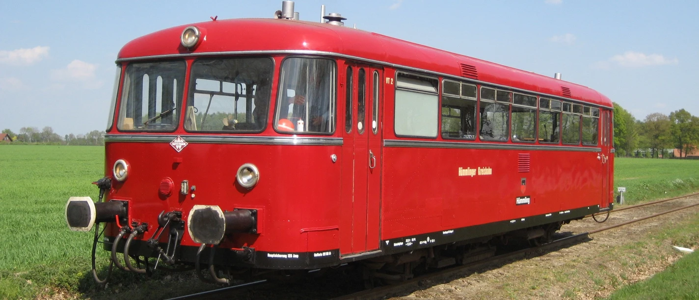 Hümmlinger Kreisbahn.jpg Roter Schienenbus der Hümmlinger Kreisbahn fährt auf eingleisiger Strecke durch grüne Landschaft.